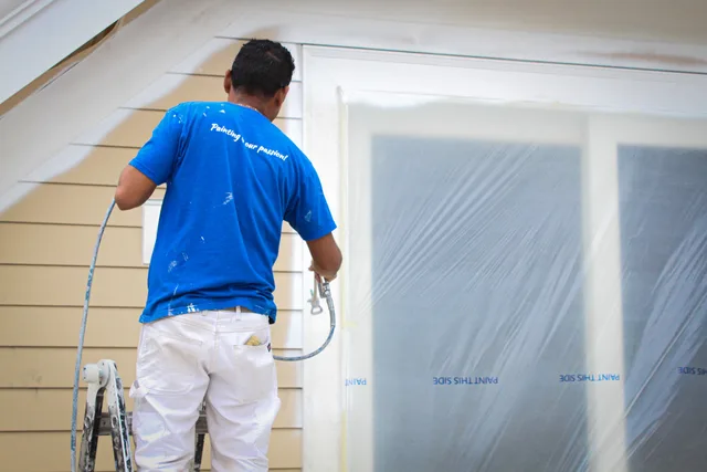 An American Town Painting painter spraying yellow siding