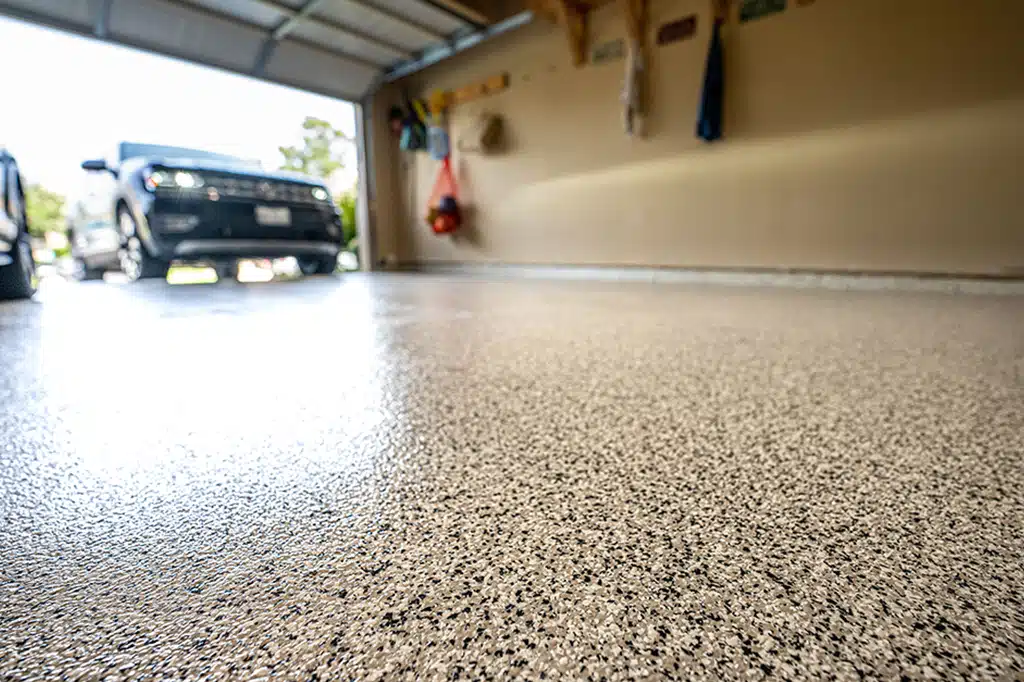 A garage featuring a white concrete floor with epoxy finish and a car parked inside, showcasing American Town Painting.