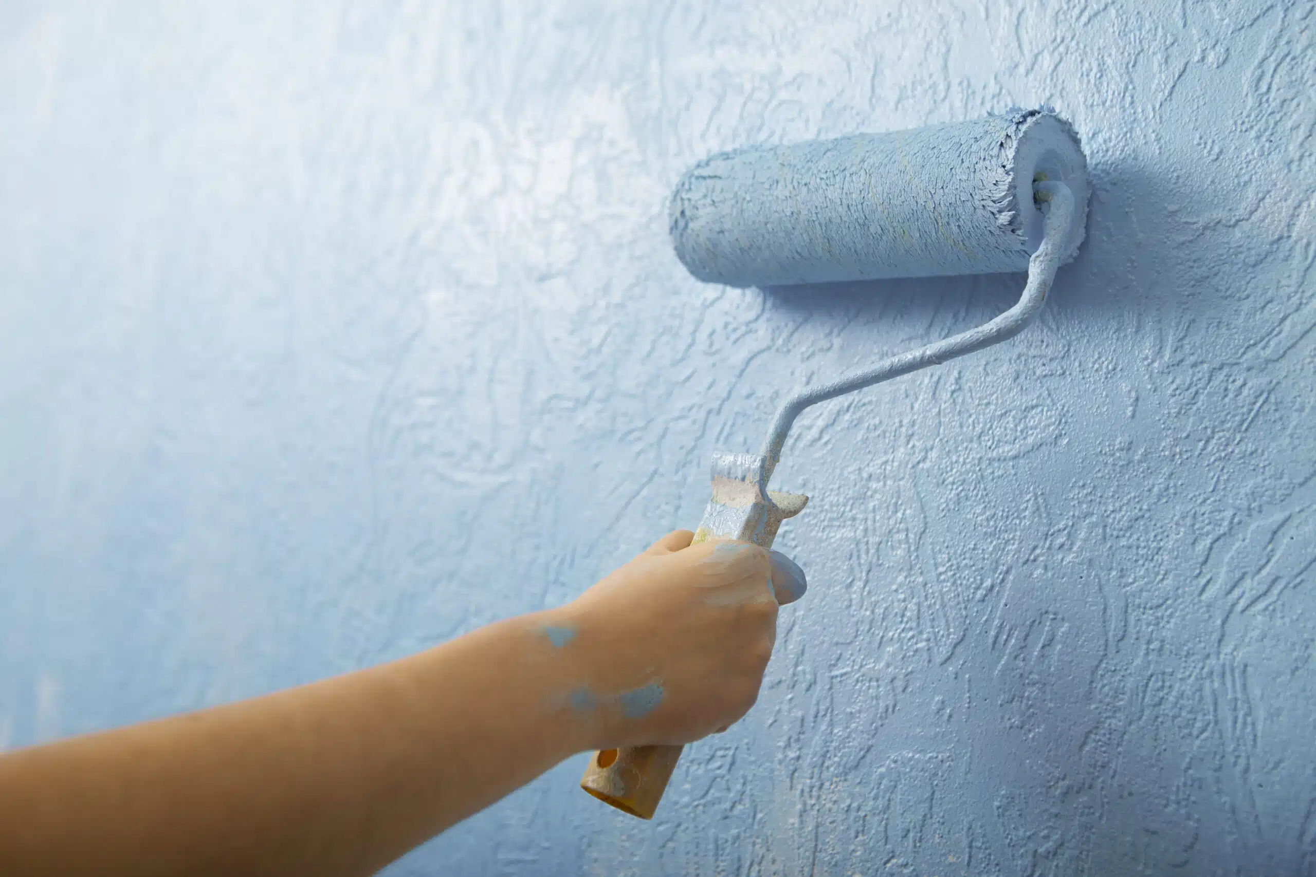 A person painting a blue wall with a roller, representing the services of American Town Painting.