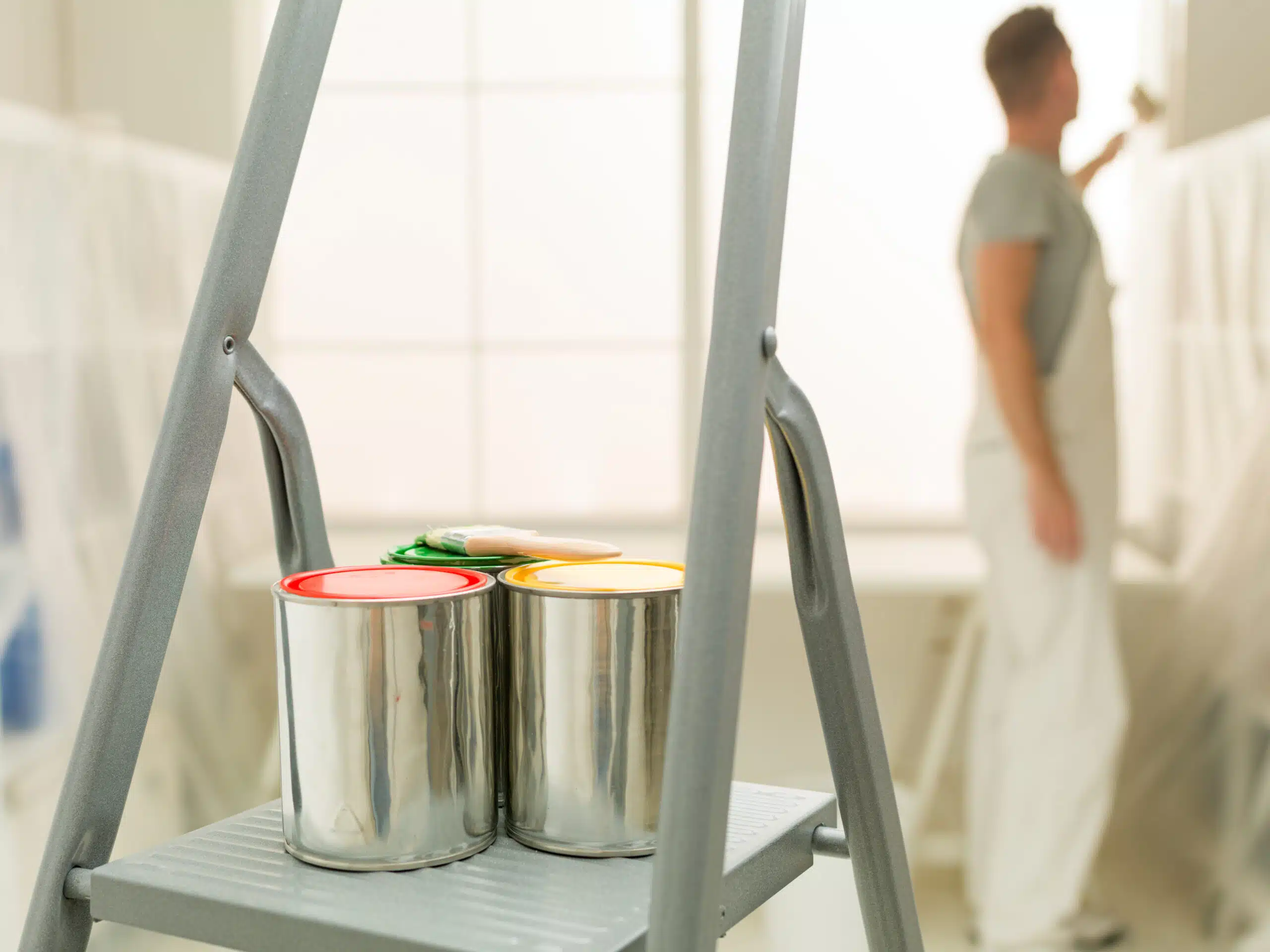 A man on a ladder holds paint cans, preparing to paint a building for American Town Painting.