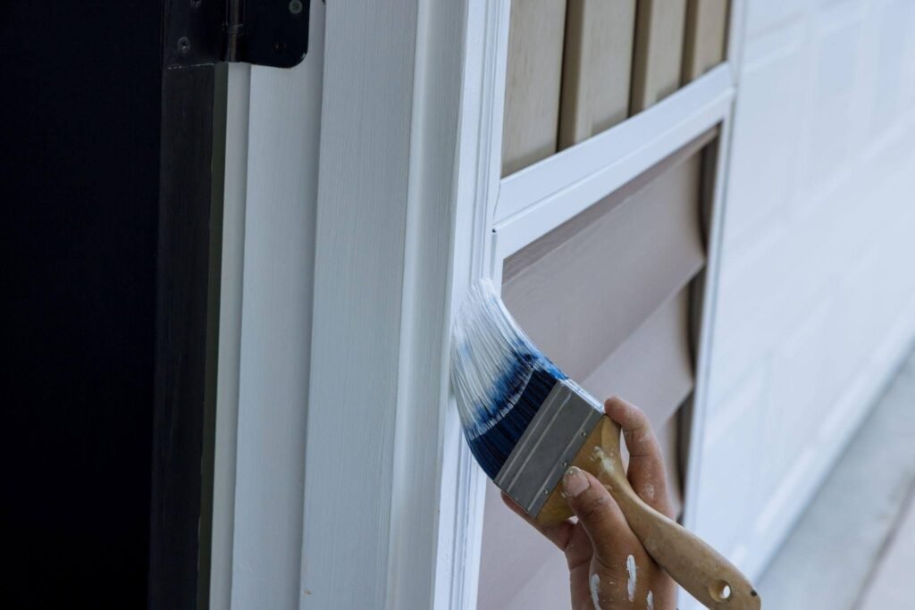 Close up of a hand using a paintbrush to apply fresh white paint to a door frame